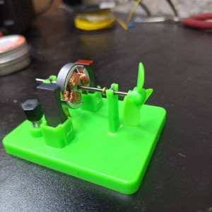 Open-frame DC motor demonstration model with exposed copper coils and green propeller